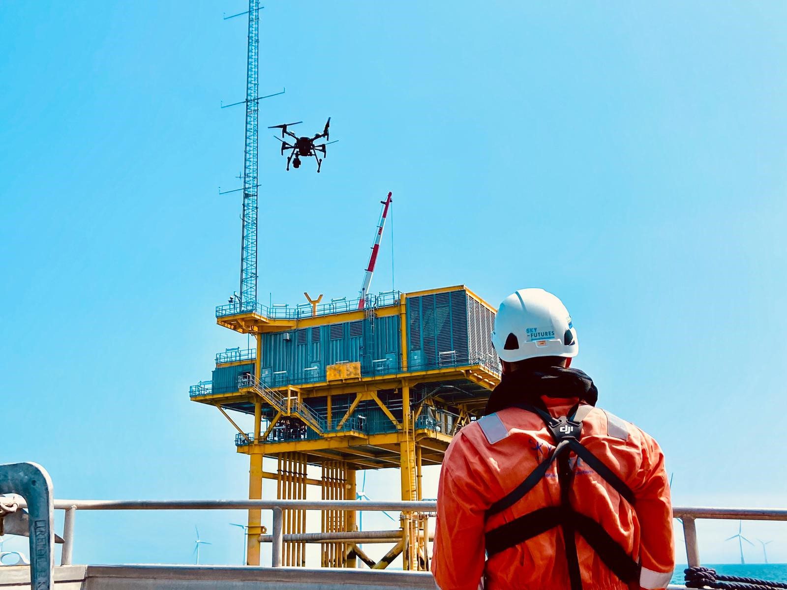 Drone inspecting substation offshore with pilot in foreground